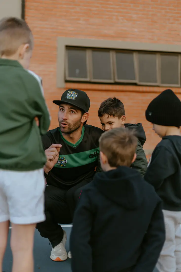 A Smash360 coach crouched at eye level, talking a group of young players through a drill.