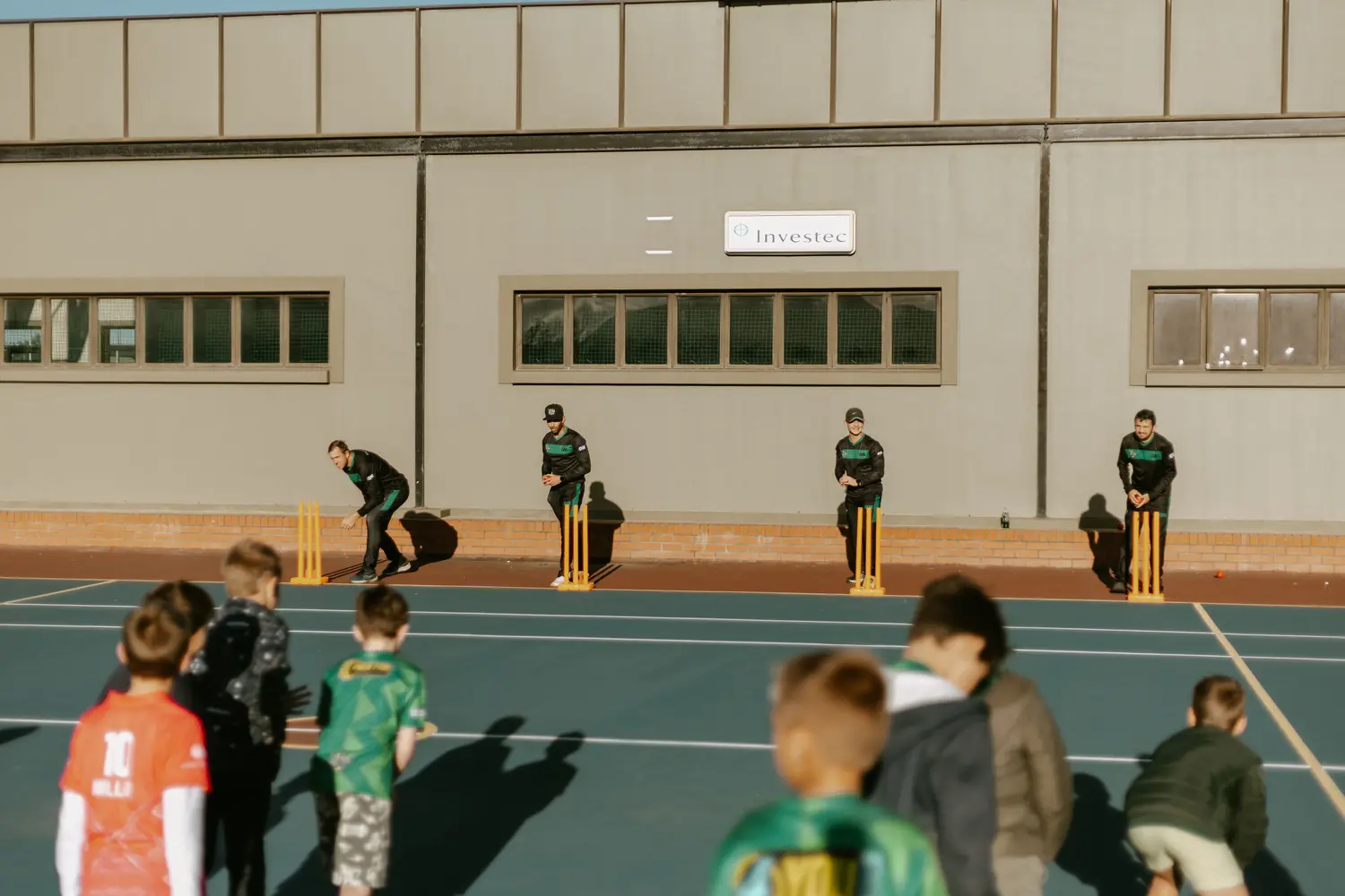 A weekday afternoon session in progress, coaches at the stumps and players waiting their turn.